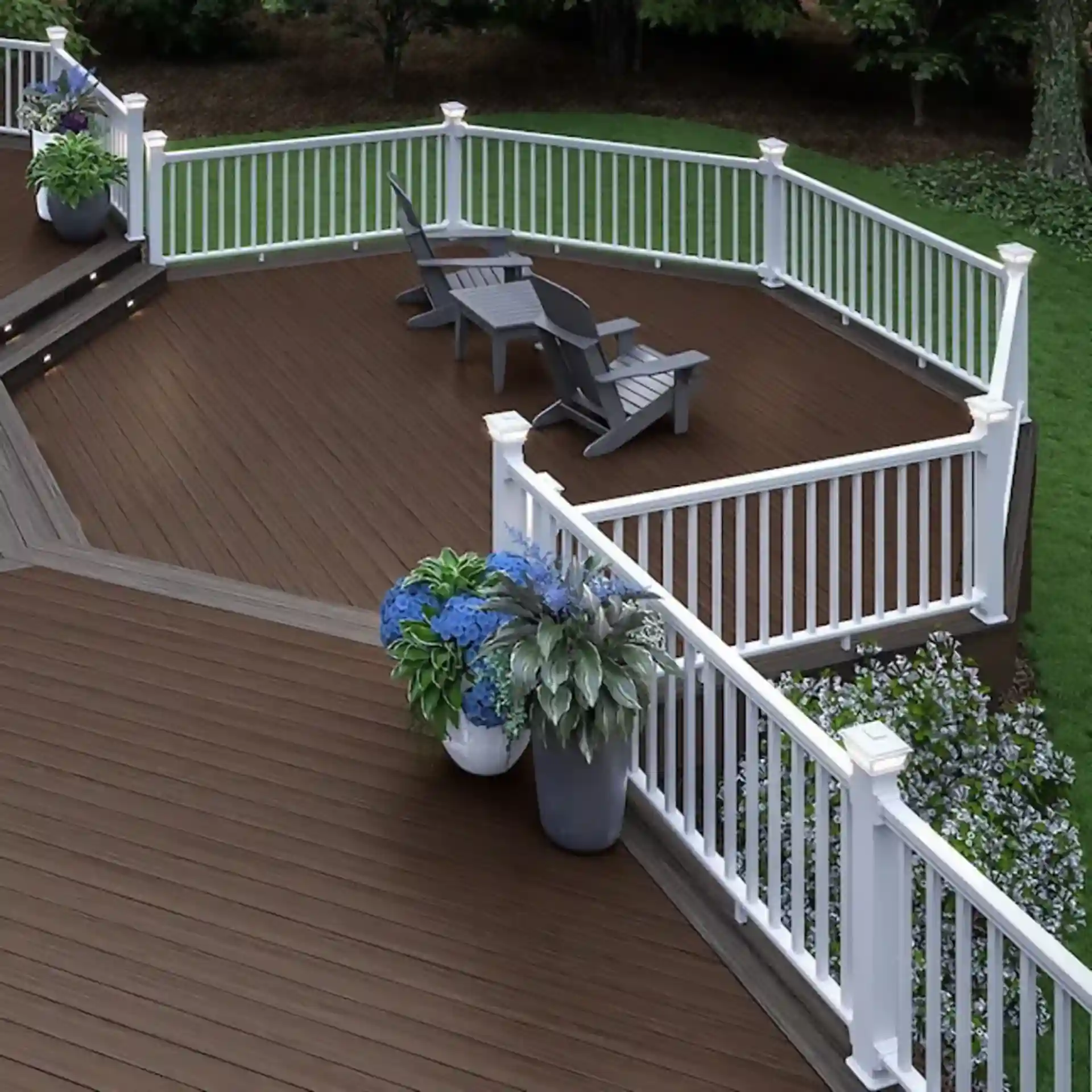 Curved deck with white railings, two chairs, and potted plants, surrounded by greenery.