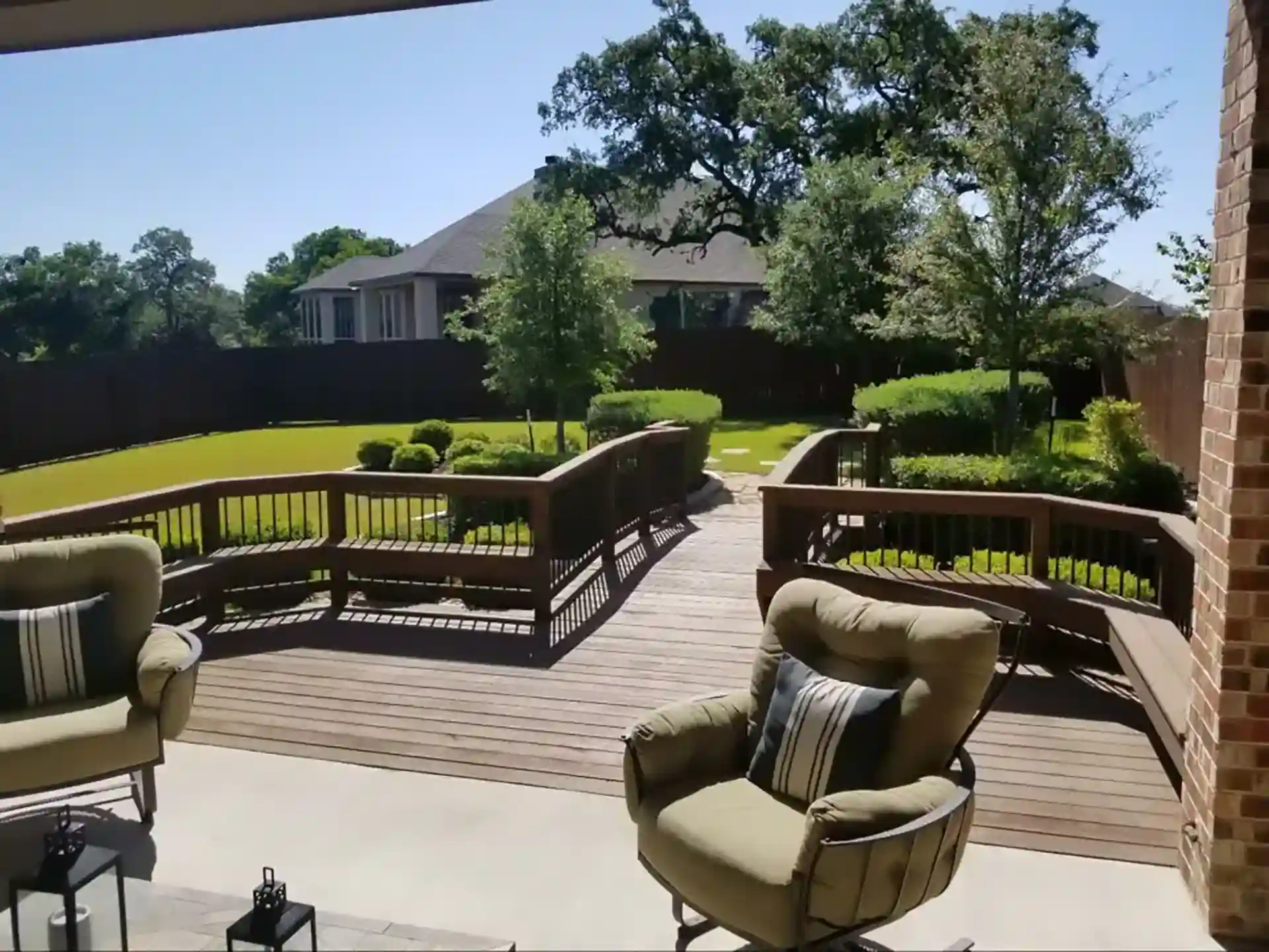 Wooden deck with curved railings, featuring two chairs and a view of a landscaped backyard with trees
