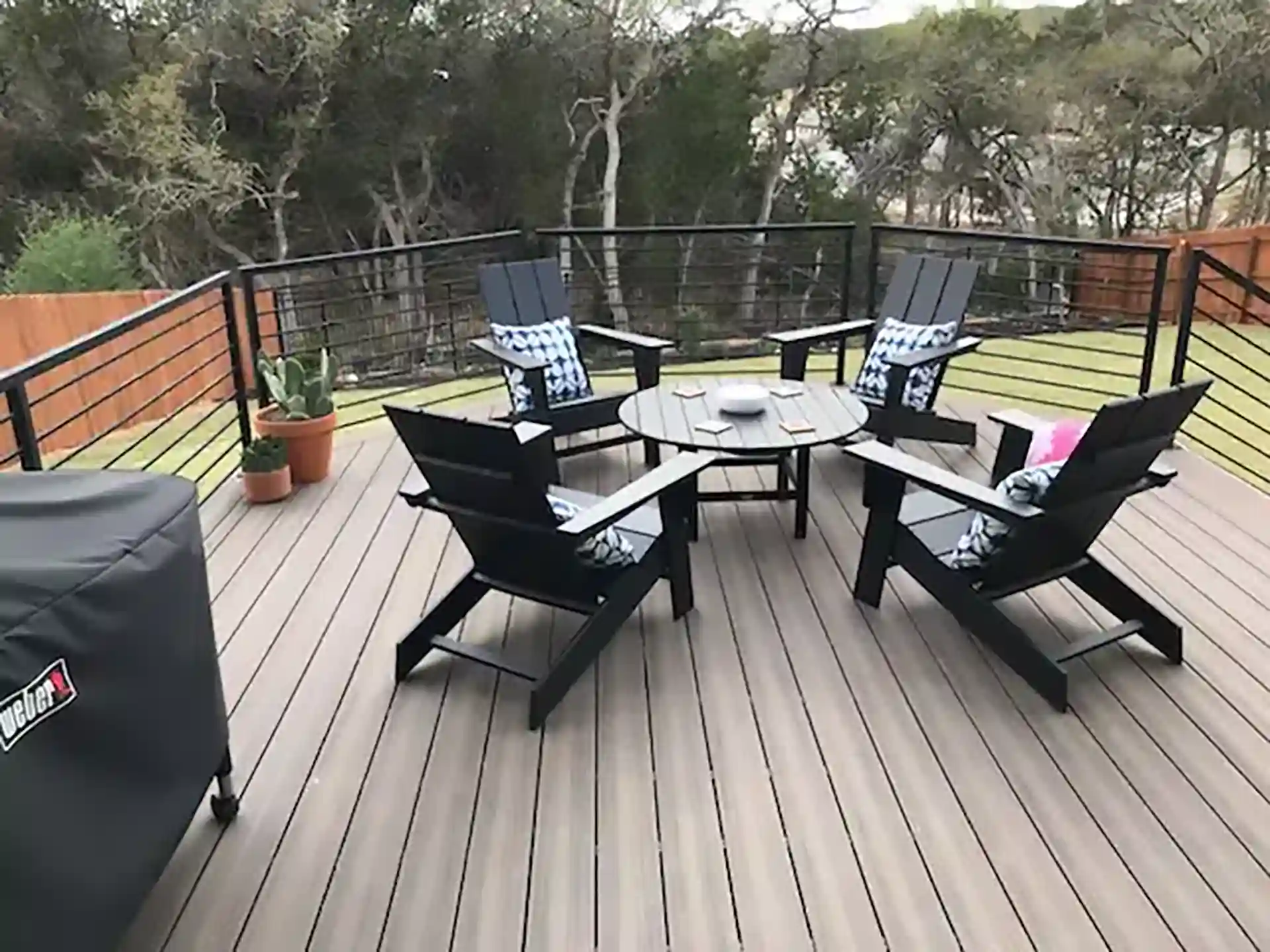 Deck with black chairs and a round table, featuring a black cable railing and surrounding greenery.