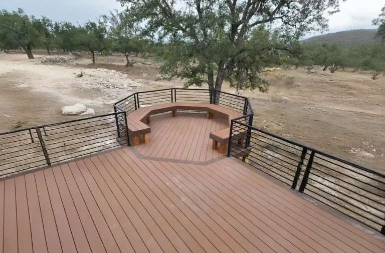 Deck with a hexagonal shape, featuring built-in wooden seating and black cable railing, surrounded by trees and a natural landscape.