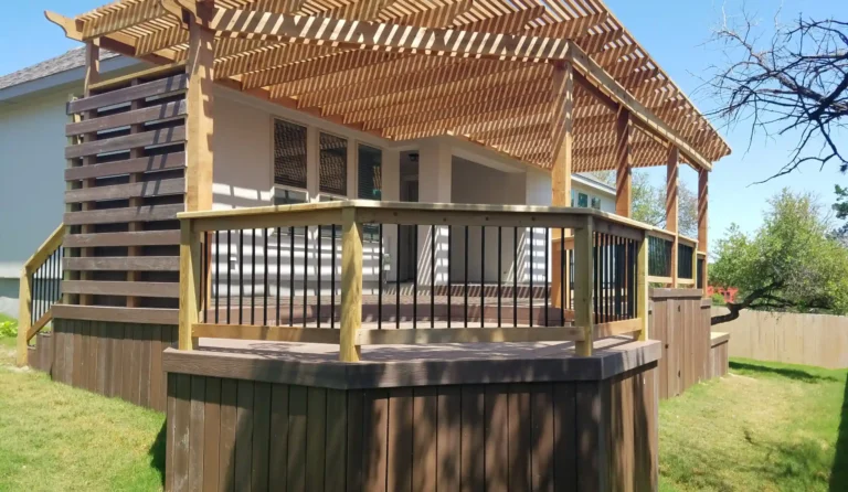 Custom wood pergola with angled rafters installed over a raised composite deck with horizontal privacy slats and metal railing.