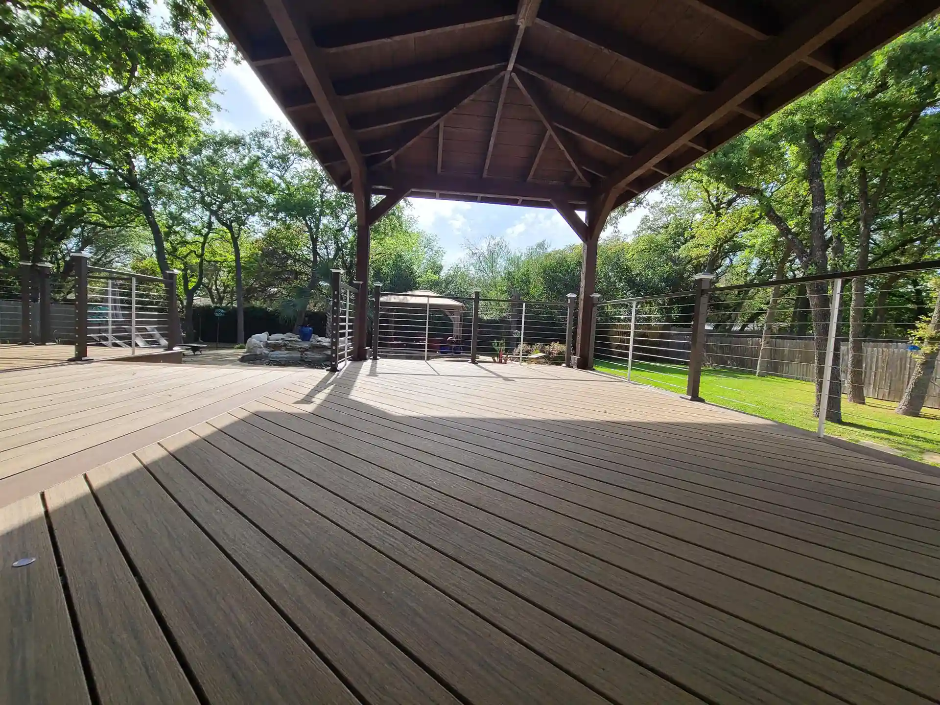 Composite deck with a wooden pavilion and cable railings overlooking a lush backyard.
