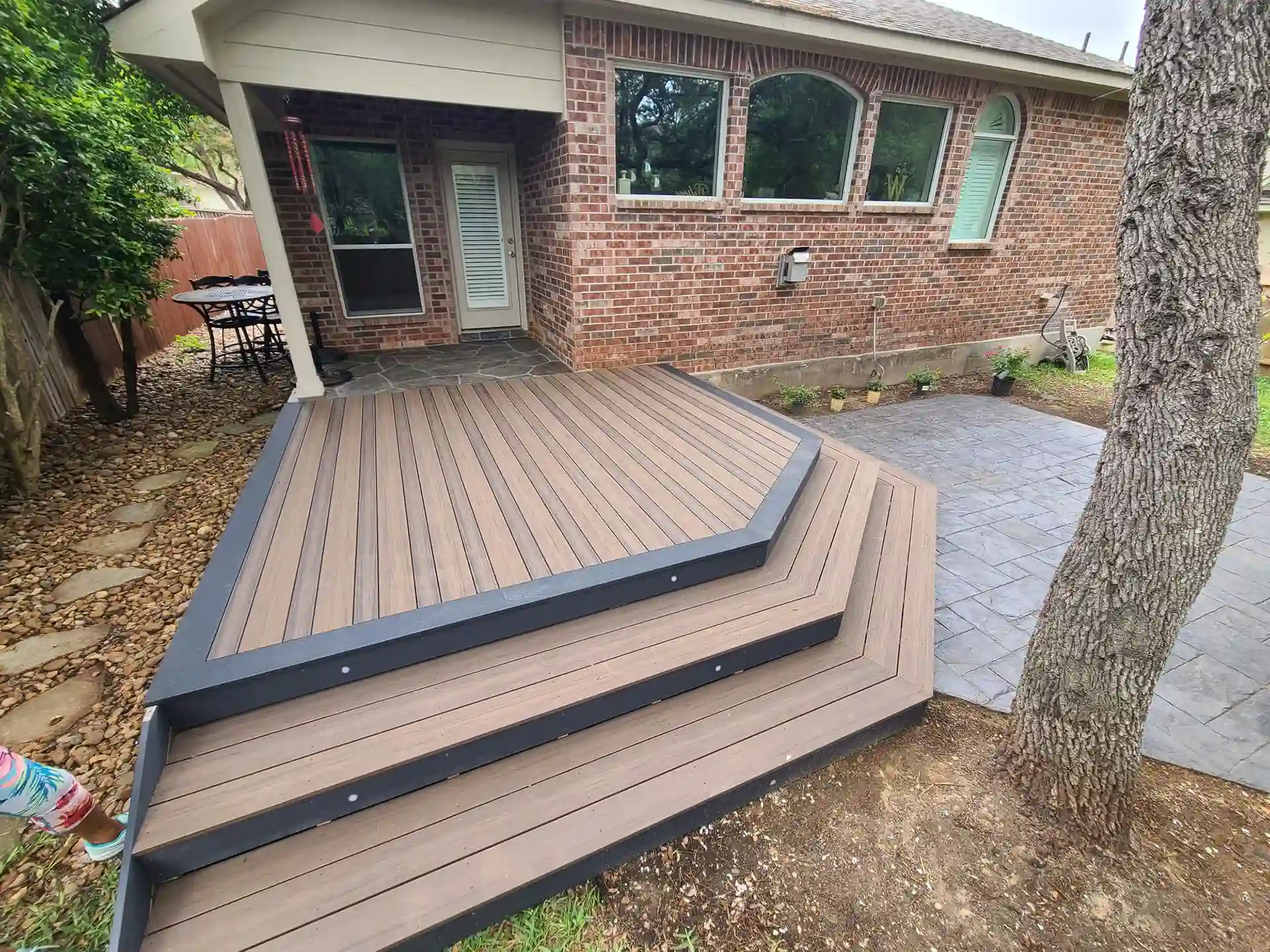 Custom composite deck with black trim and steps, adjacent to a stone patio and brick house.