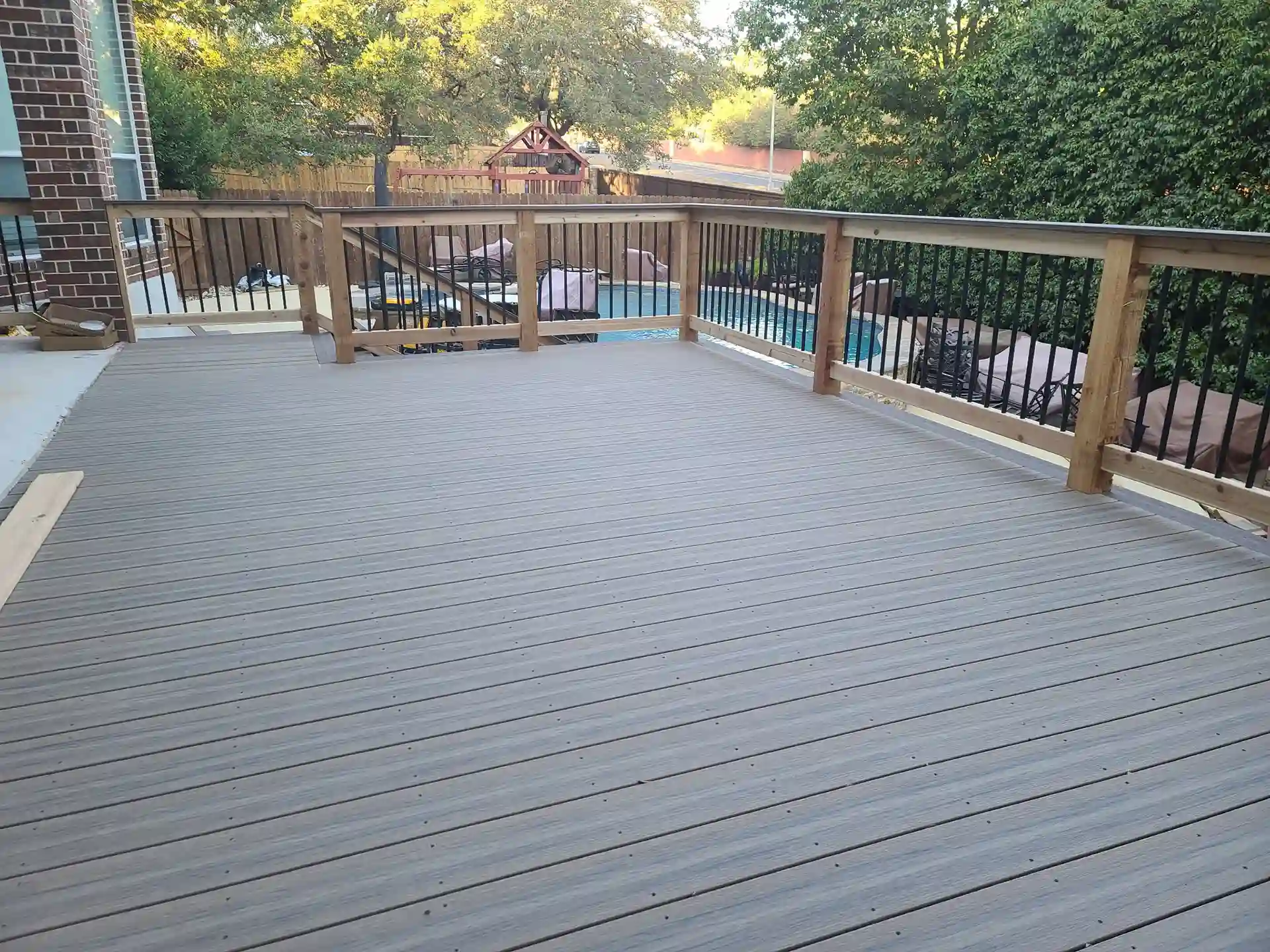 Finished composite deck with wooden railing and metal spindles, overlooking a pool area.