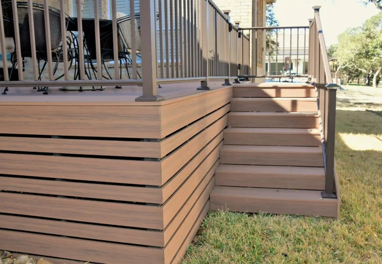 Raised composite deck with horizontal slat skirting, matching stairs, and metal railing, built over a grass lawn.